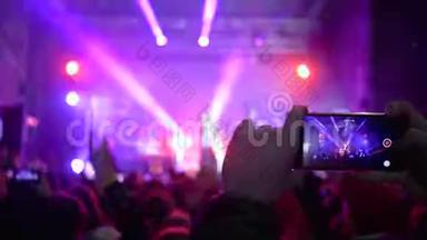 歌迷们手里拿着手机，在明亮的现场灯光下欣赏摇滚音乐会的现场音乐